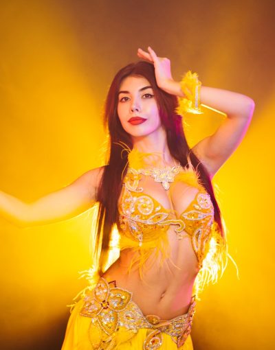 Alluring sexy traditional oriental belly dancer girl dancing on yellow neon smoke background.