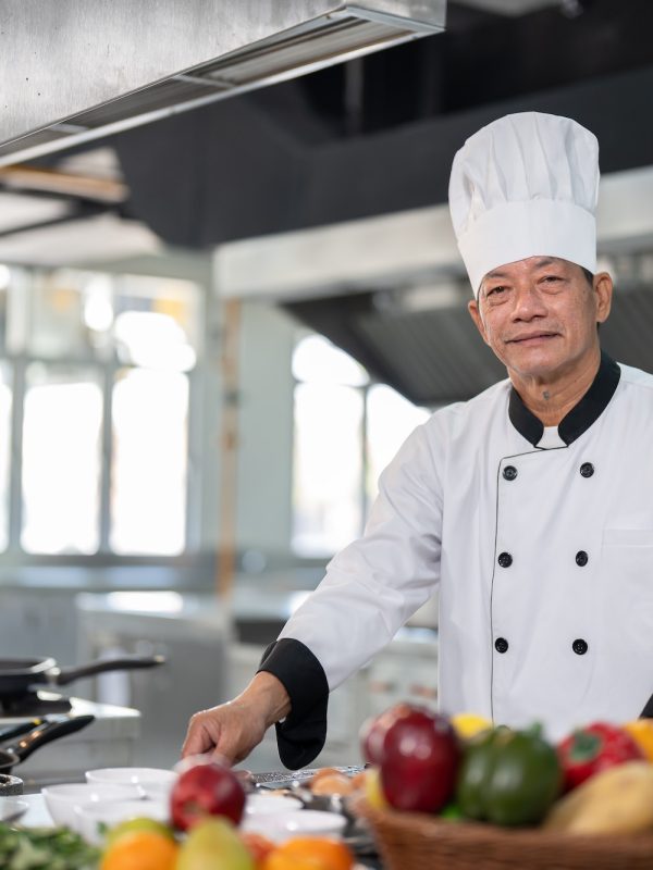 Senior Asian chef man in dress uniform preparing meal with various vegetables in kitchen restaurant